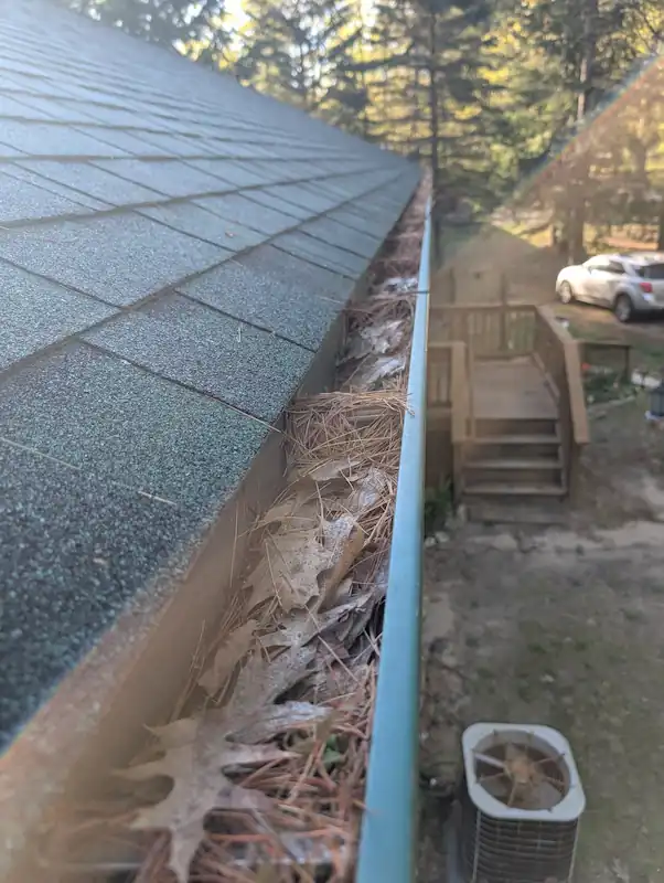 Clogged gutter full of leaves and debris before cleaning — seasonal maintenance visit in Honor, MI